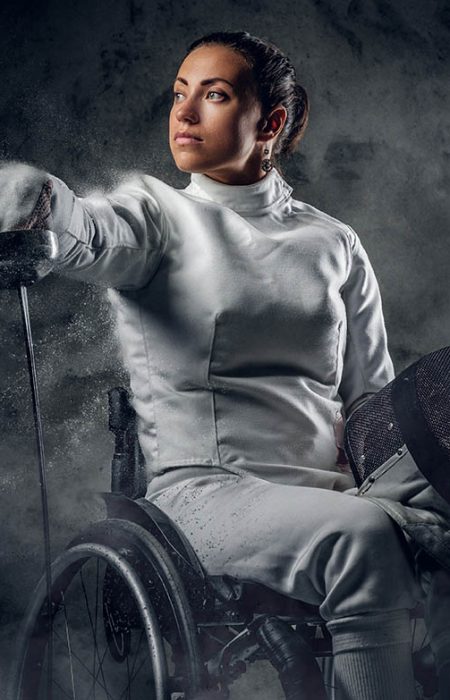 Female fencer in wheelchair with safety mask of a face holding rapier, dust effect on image.