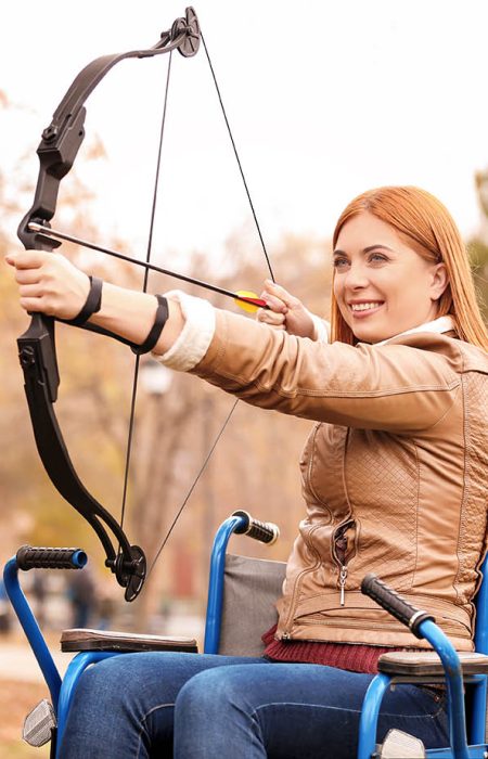 Young woman in wheelchair practicing archery outdoors